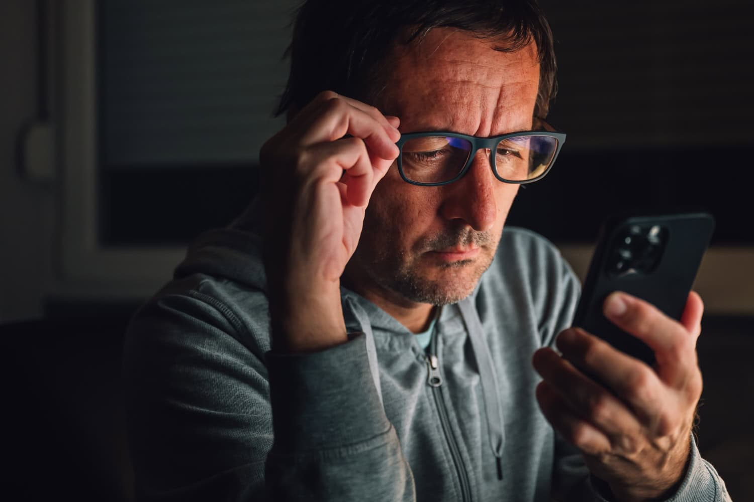 Bored man using smartphone late at night, browsing the internet or using social media apps