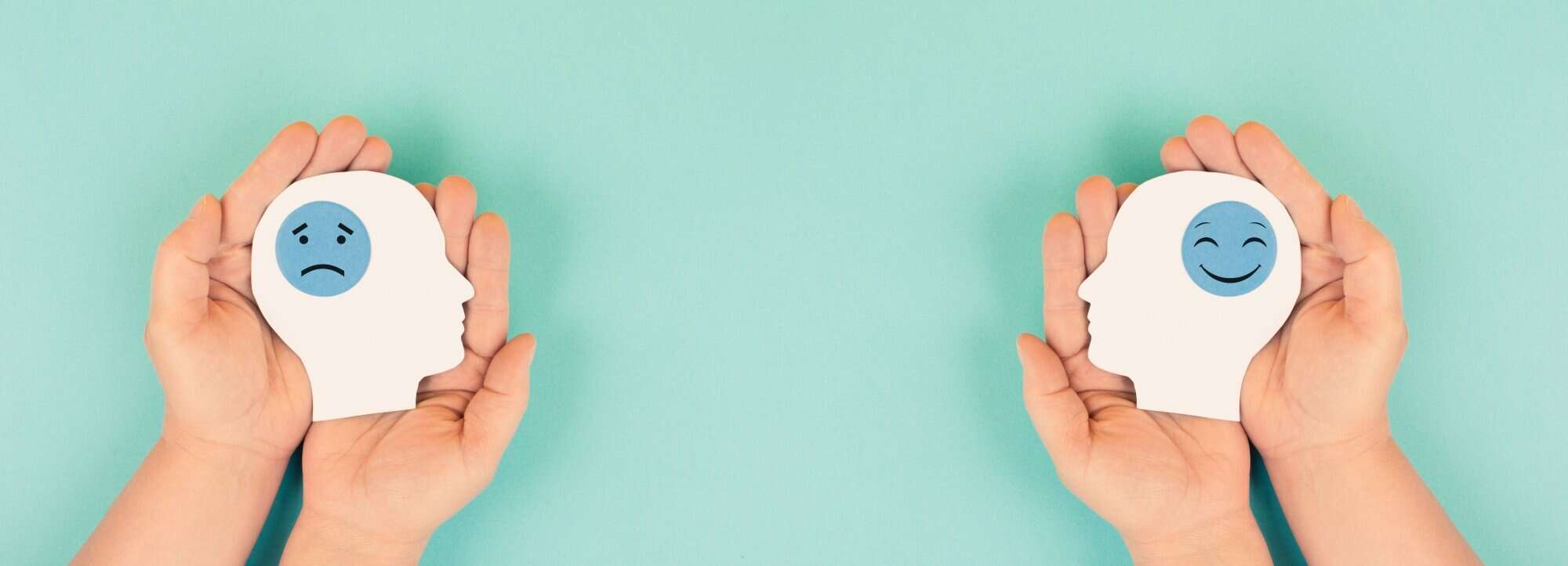 hands holding cutouts of head symbolizing happy sad emotions, concept of bipolar disorder