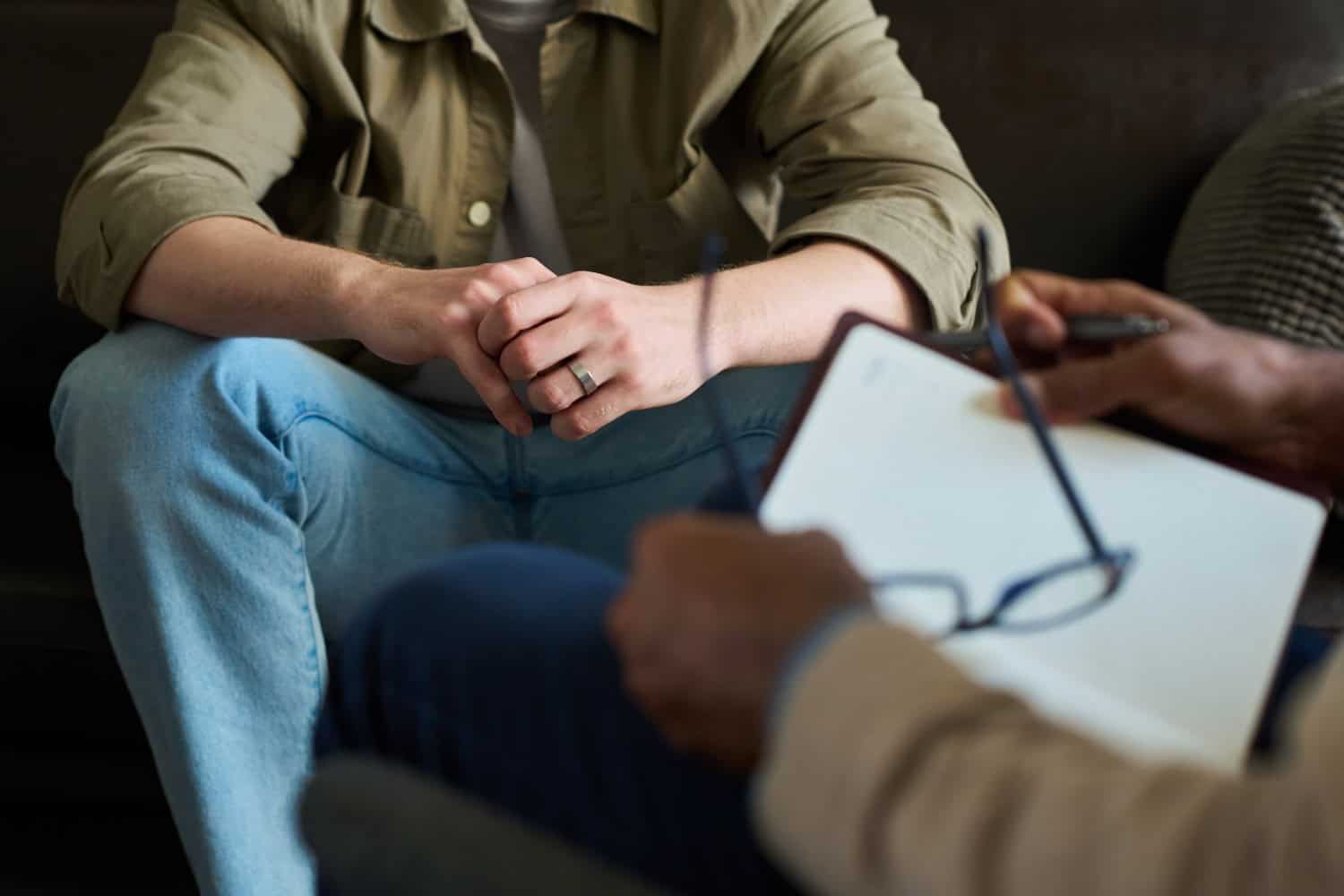 Two adults sit indoors with one taking notes as the other talks, counseling or therapy concept