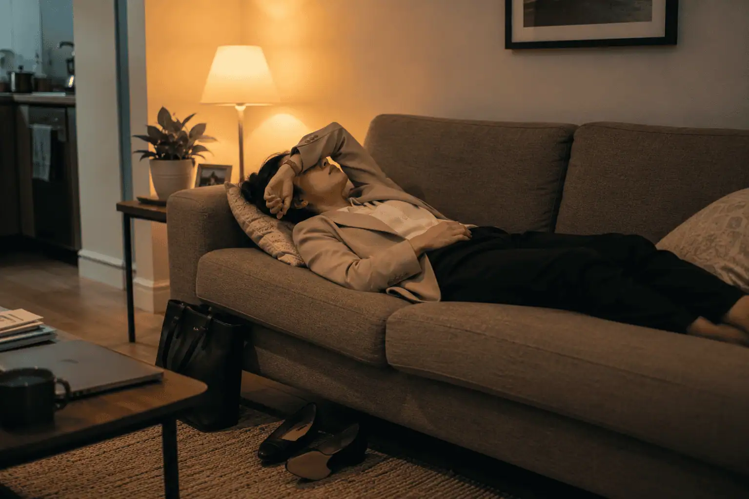 a young professional lying on a couch after work, conveying physical and emotional exhaustion